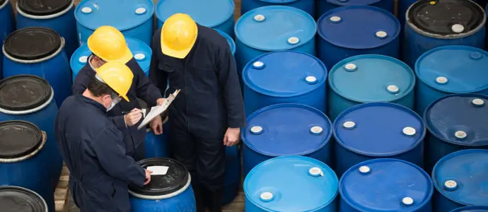 Workers in coveralls inspect shipment of barrels
