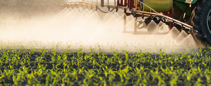 Farm tractor spraying chlorpyrifos onto corn crops